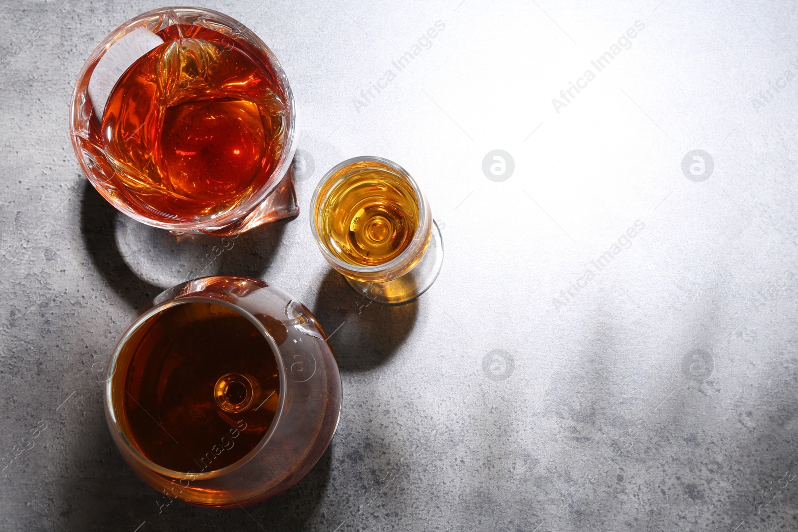 Photo of Different delicious liqueurs in glasses on grey table, flat lay. Space for text