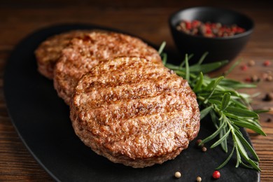 Photo of Slate plate with tasty grilled hamburger patties and seasonings on wooden table, closeup