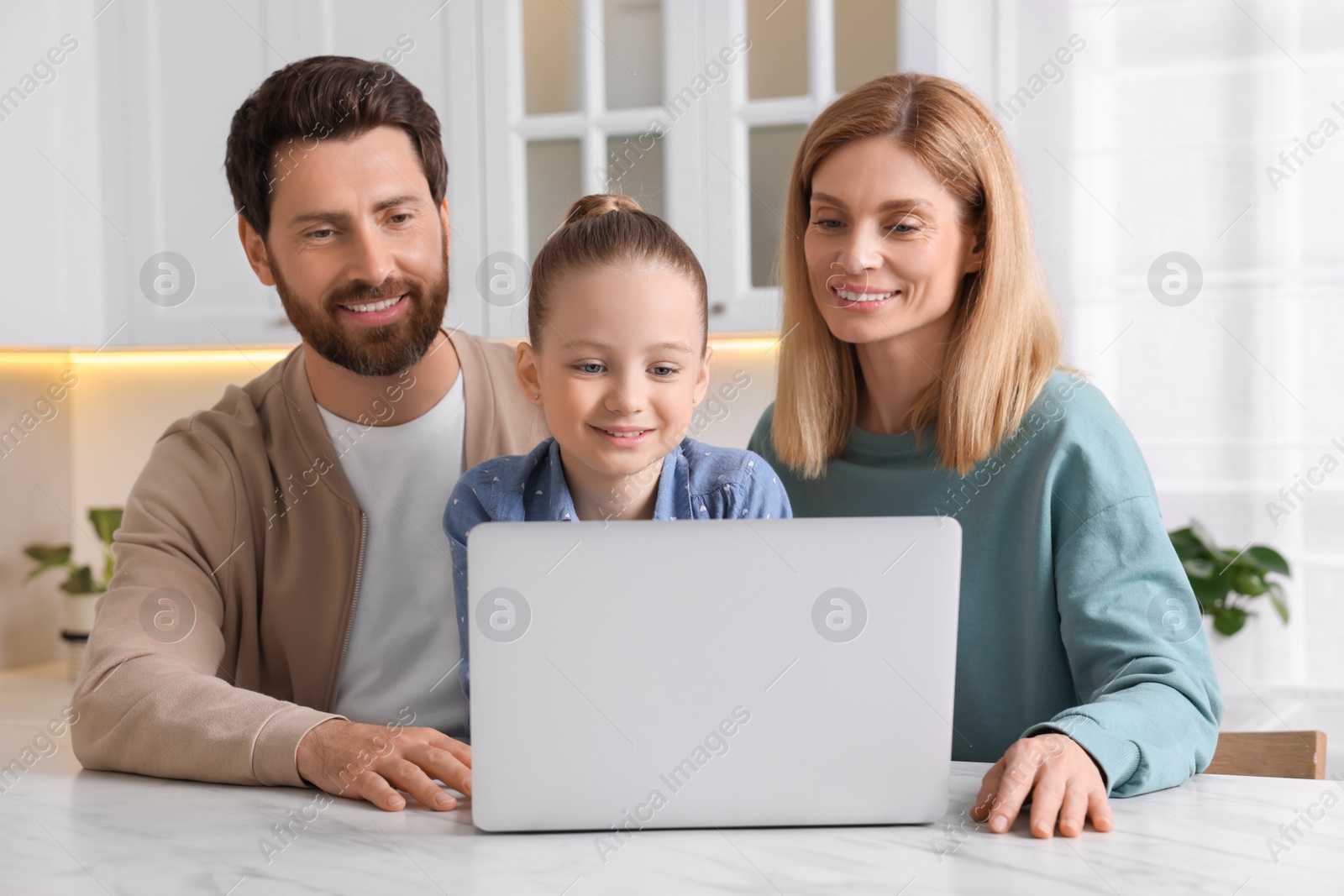 Photo of Happy family with laptop at white table indoors