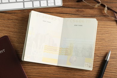 Photo of Moldova, Ceadir-Lunga - June 13, 2022: Passport with blank visa pages, pen, glasses and keyboard on wooden table, flat lay