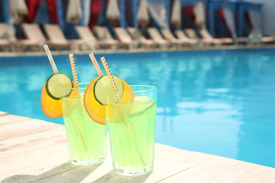 Refreshing cocktail in glasses near outdoor swimming pool on sunny day. Space for text