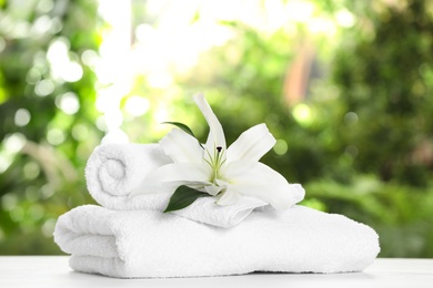 Photo of Soft bath towels and flower on table against blurred background