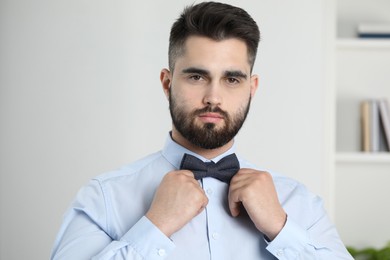 Photo of Portrait of handsome man adjusting bow tie indoors