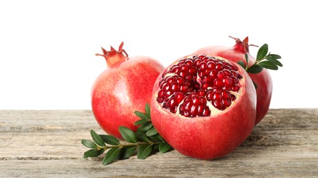 Fresh pomegranates and green leaves on wooden table against white background