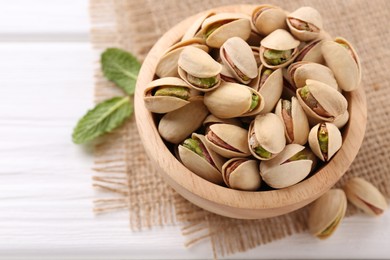 Photo of Tasty pistachios in bowl on white wooden table, closeup. Space for text