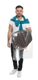 Photo of Man holding garment cover with clothes on white background. Dry-cleaning service