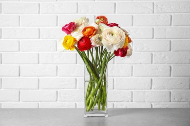 Photo of Vase with beautiful spring ranunculus flowers on table near brick wall