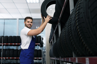 Photo of Male mechanic with car tire in auto store