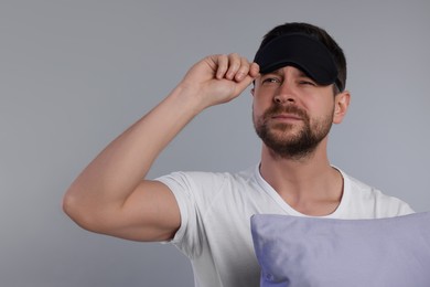 Photo of Sleepy man with pillow and mask on grey background, space for text. Insomnia problem