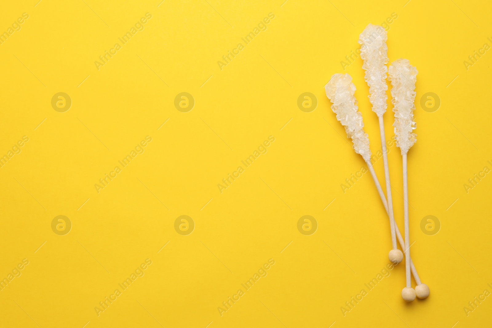 Photo of Wooden sticks with sugar crystals and space for text on yellow background, flat lay. Tasty rock candies