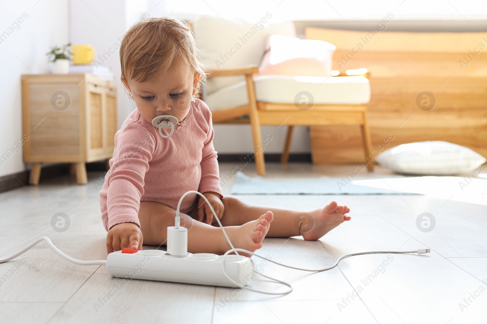 Photo of Cute baby playing with power strip on floor at home. Dangerous situation