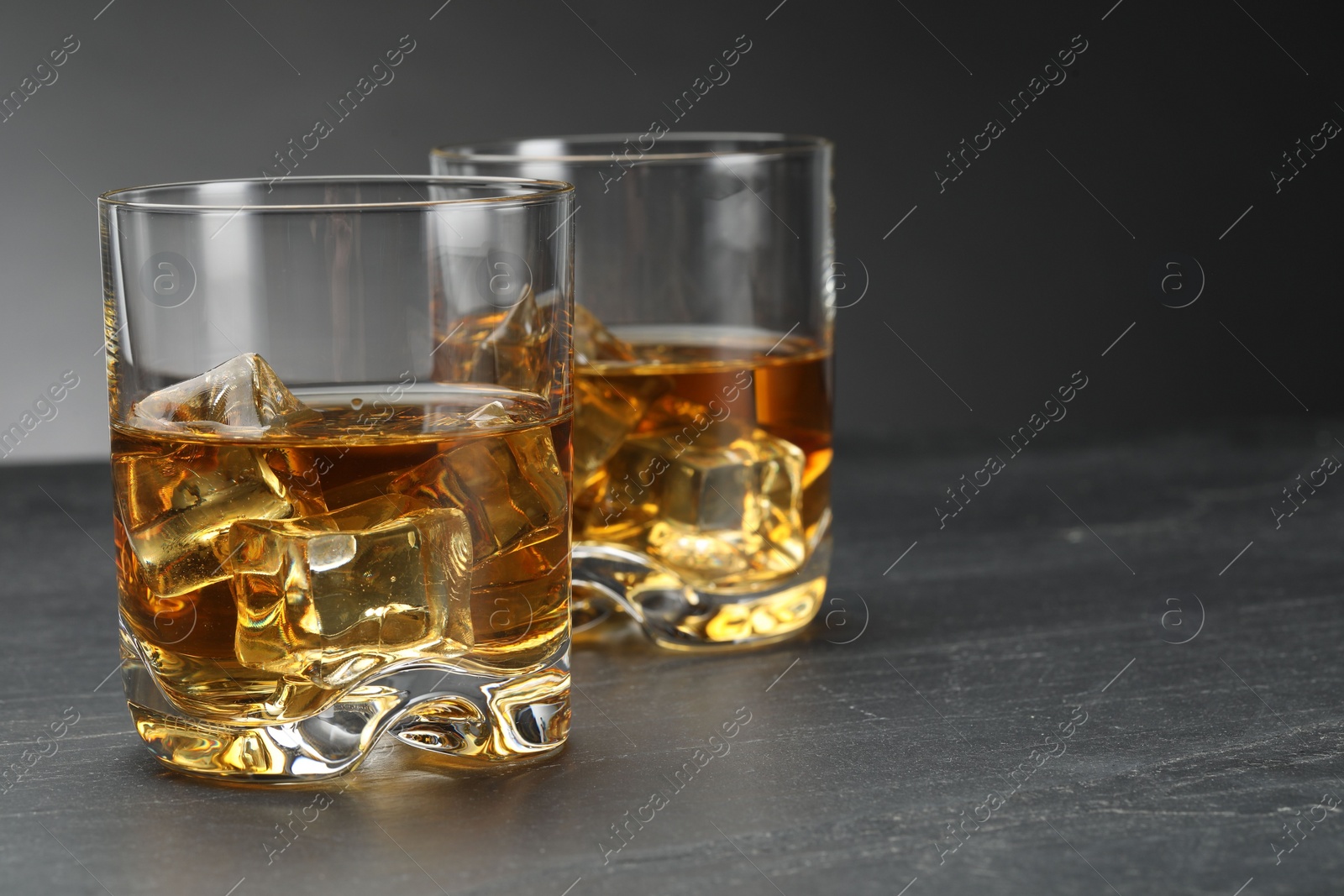 Photo of Whiskey and ice cubes in glasses on grey table, closeup. Space for text