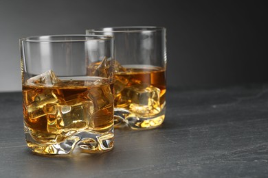 Whiskey and ice cubes in glasses on grey table, closeup. Space for text