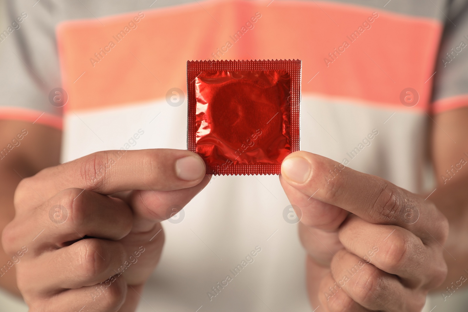 Photo of Young man holding red condom, closeup. Safe sex concept