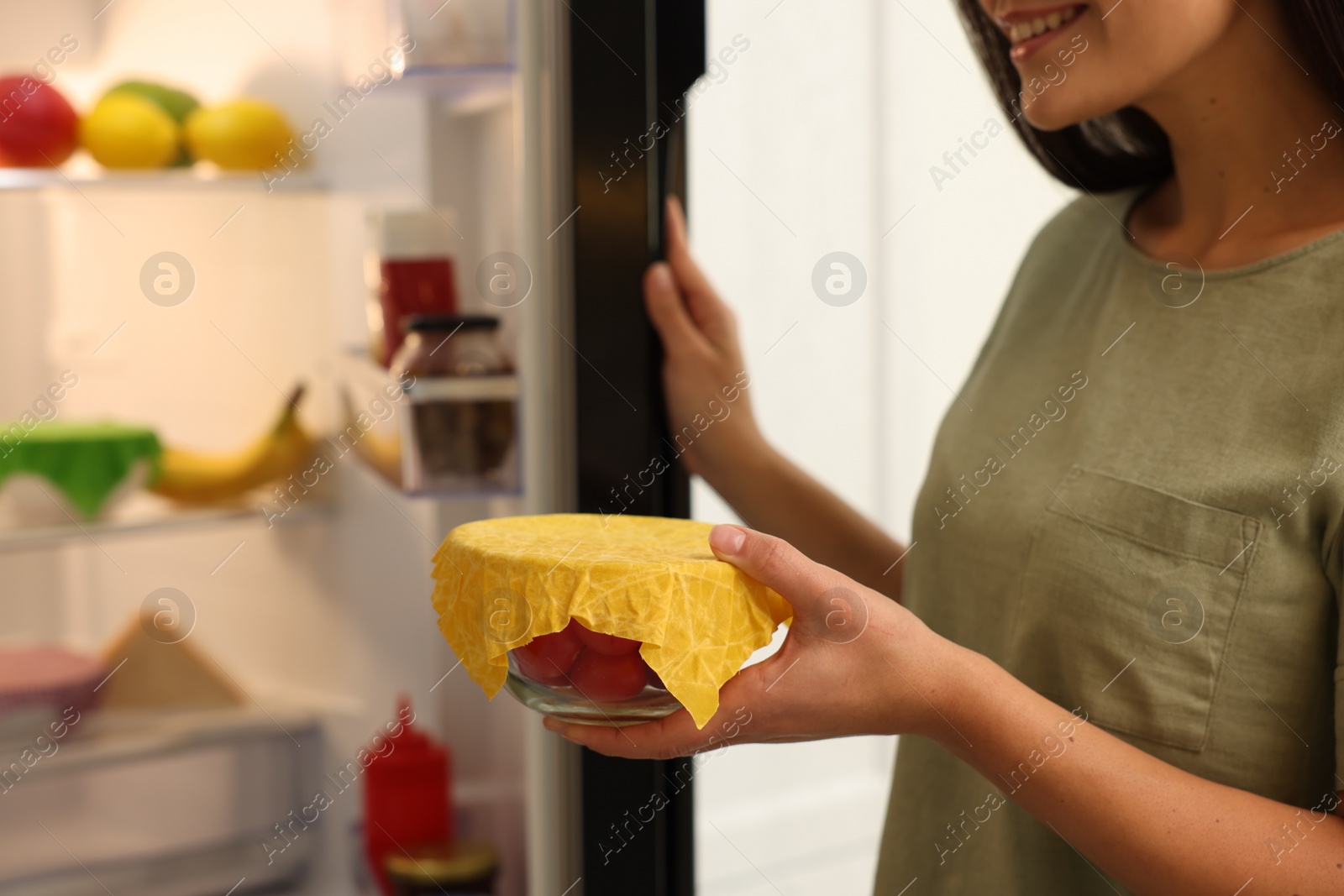 Photo of Woman holding bowl of fresh tomatoes covered with beeswax food wrap in kitchen, closeup