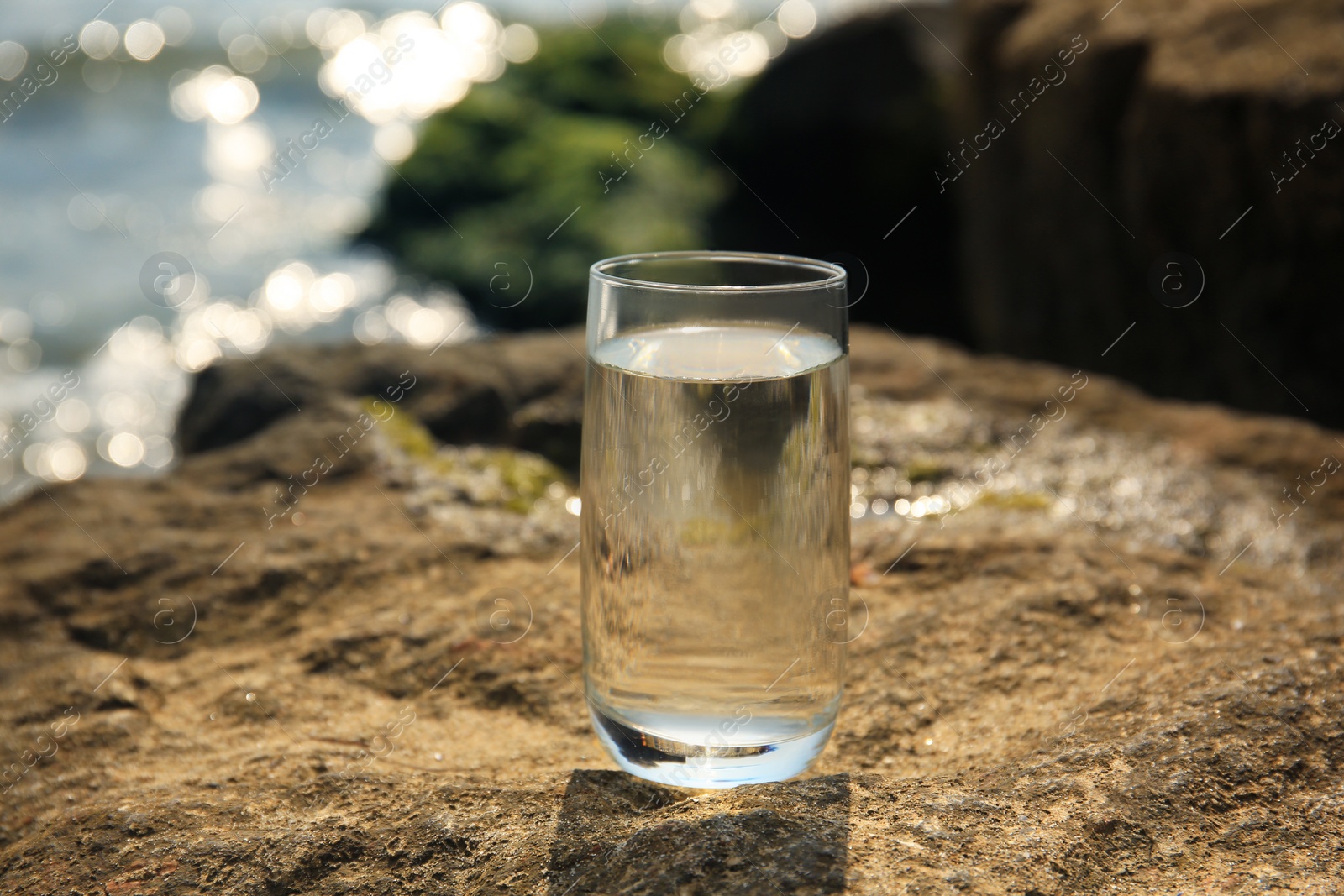 Photo of Glass of fresh water on stone near sea