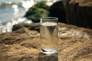 Glass of fresh water on stone near sea