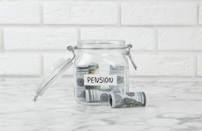 Photo of Glass jar with word Pension and banknotes on white marble table