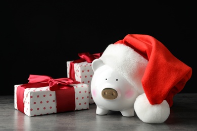 Piggy bank with Santa hat and gift boxes on grey table against black background