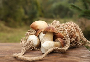 Photo of String bag and fresh wild mushrooms on wooden table outdoors, closeup