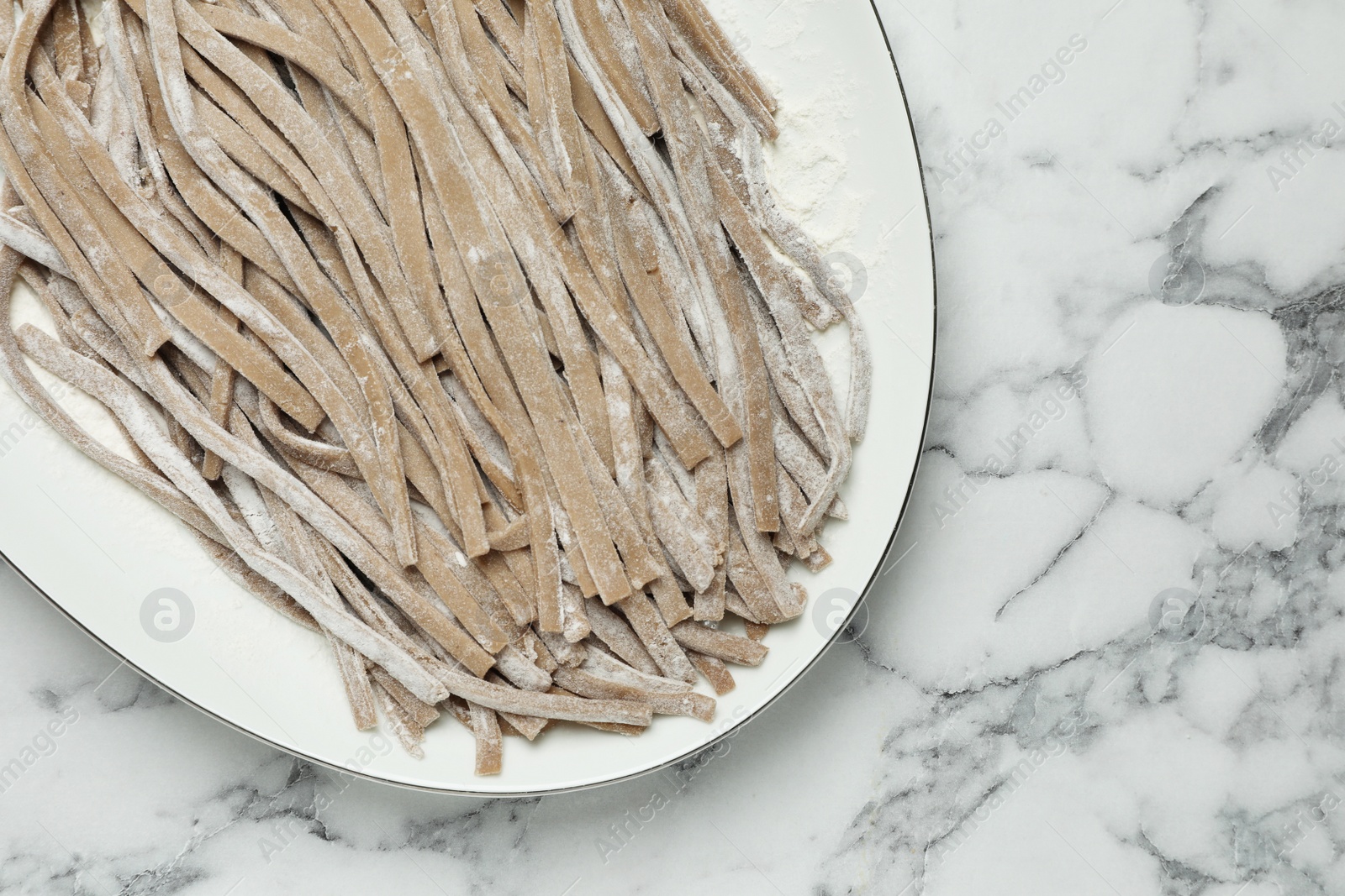 Photo of Uncooked homemade soba (buckwheat noodles) on white marble table, top view