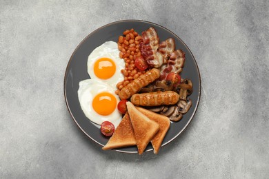 Photo of Plate with fried eggs, sausages, mushrooms, beans, bacon and toasted bread on grey table, top view. Traditional English breakfast