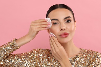 Beautiful woman removing makeup with cotton pads on pink background