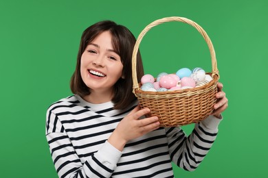 Easter celebration. Happy woman with wicker basket full of painted eggs on green background