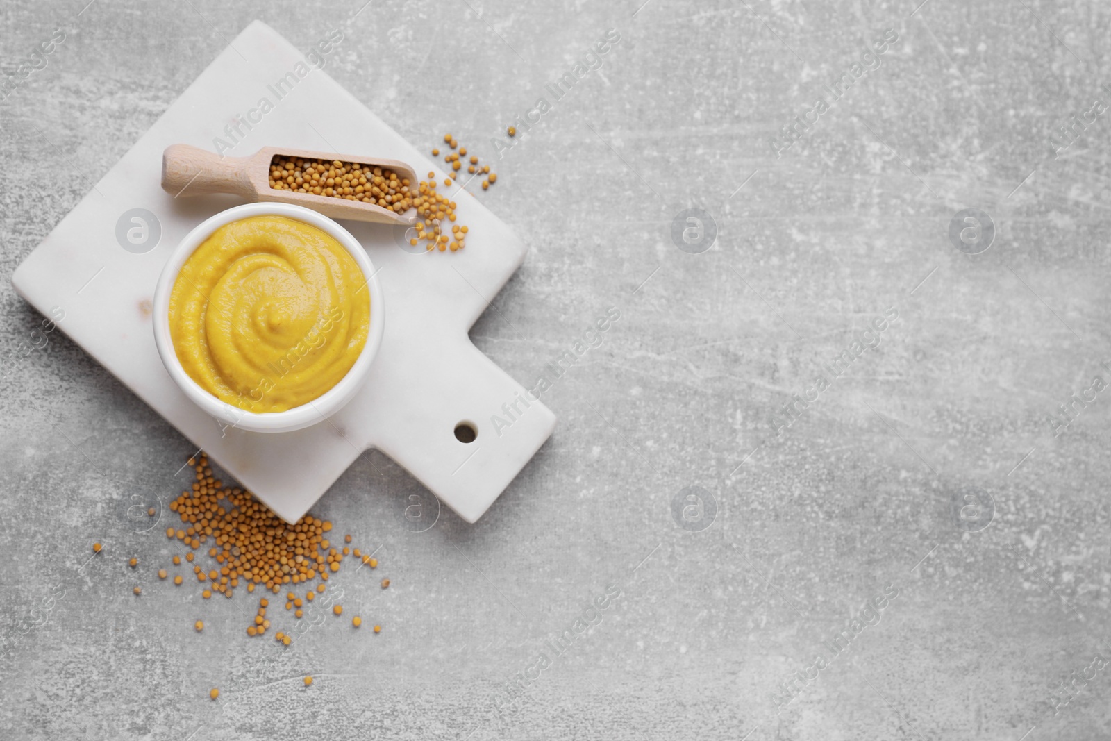 Photo of Bowl of delicious mustard and scoop with seeds on light grey table, flat lay. Space for text