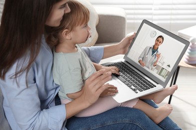 Image of Mother and daughter having online consultation with pediatrician via laptop on sofa at home