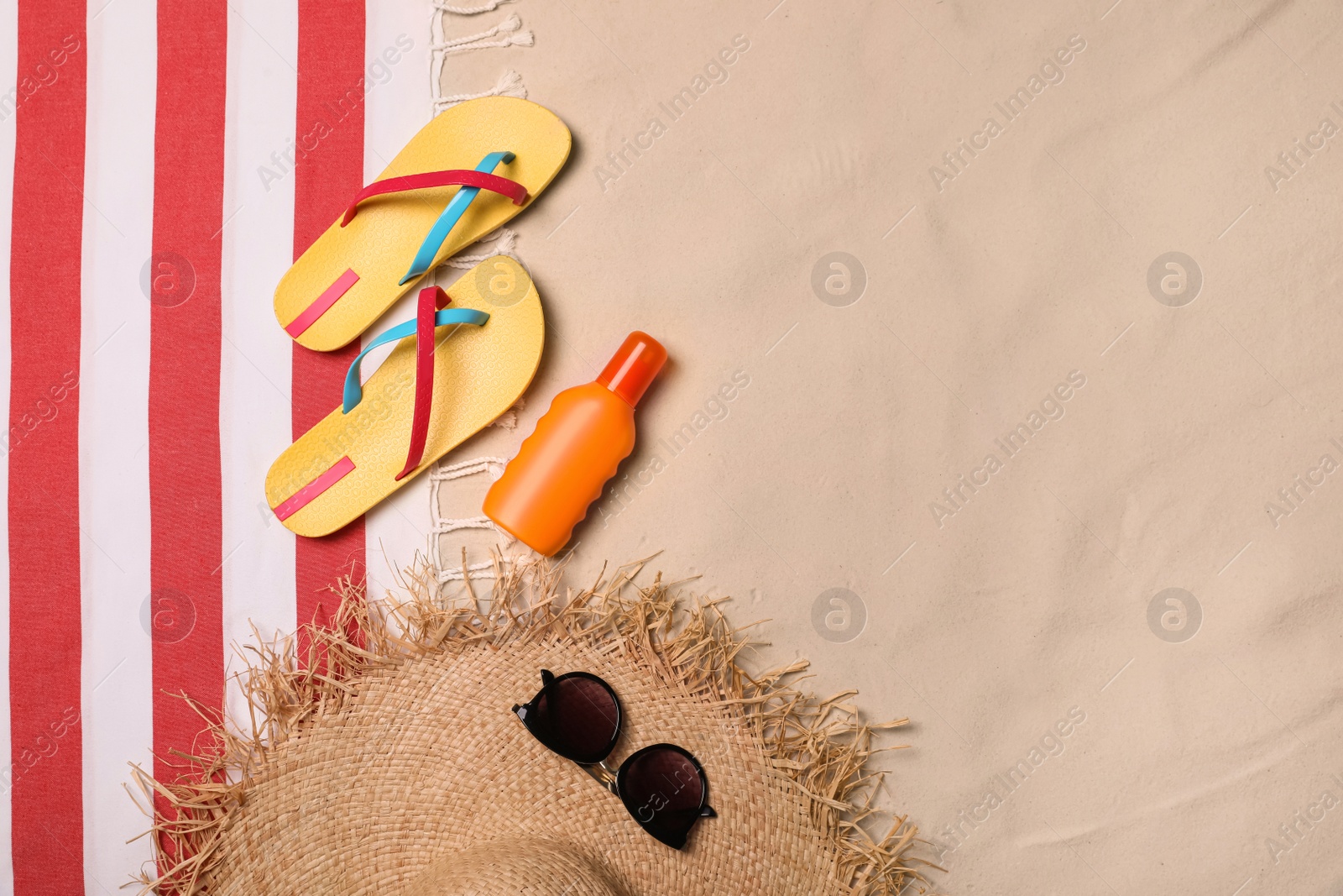 Photo of Beach towel, hat, sunglasses, sunscreen and flip flops on sand, flat lay. Space for text