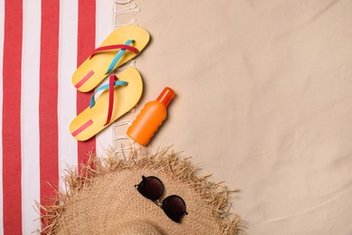 Beach towel, hat, sunglasses, sunscreen and flip flops on sand, flat lay. Space for text