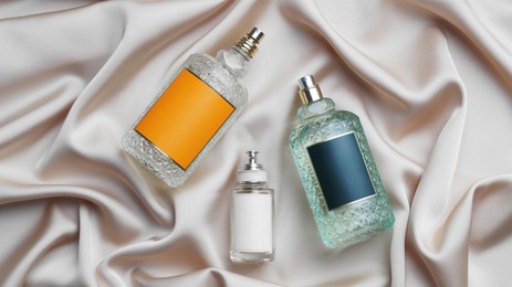 Photo of Luxury bottles of perfume on beige silk, flat lay