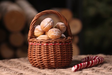 Photo of Wicker basket with delicious nut shaped cookies and candy cane on knitted fabric, closeup