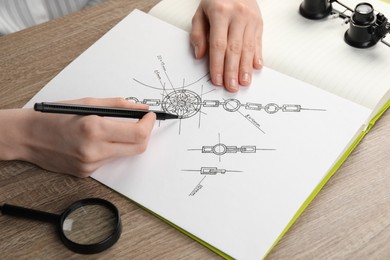 Jeweler drawing sketch of elegant bracelet on paper at wooden table, closeup