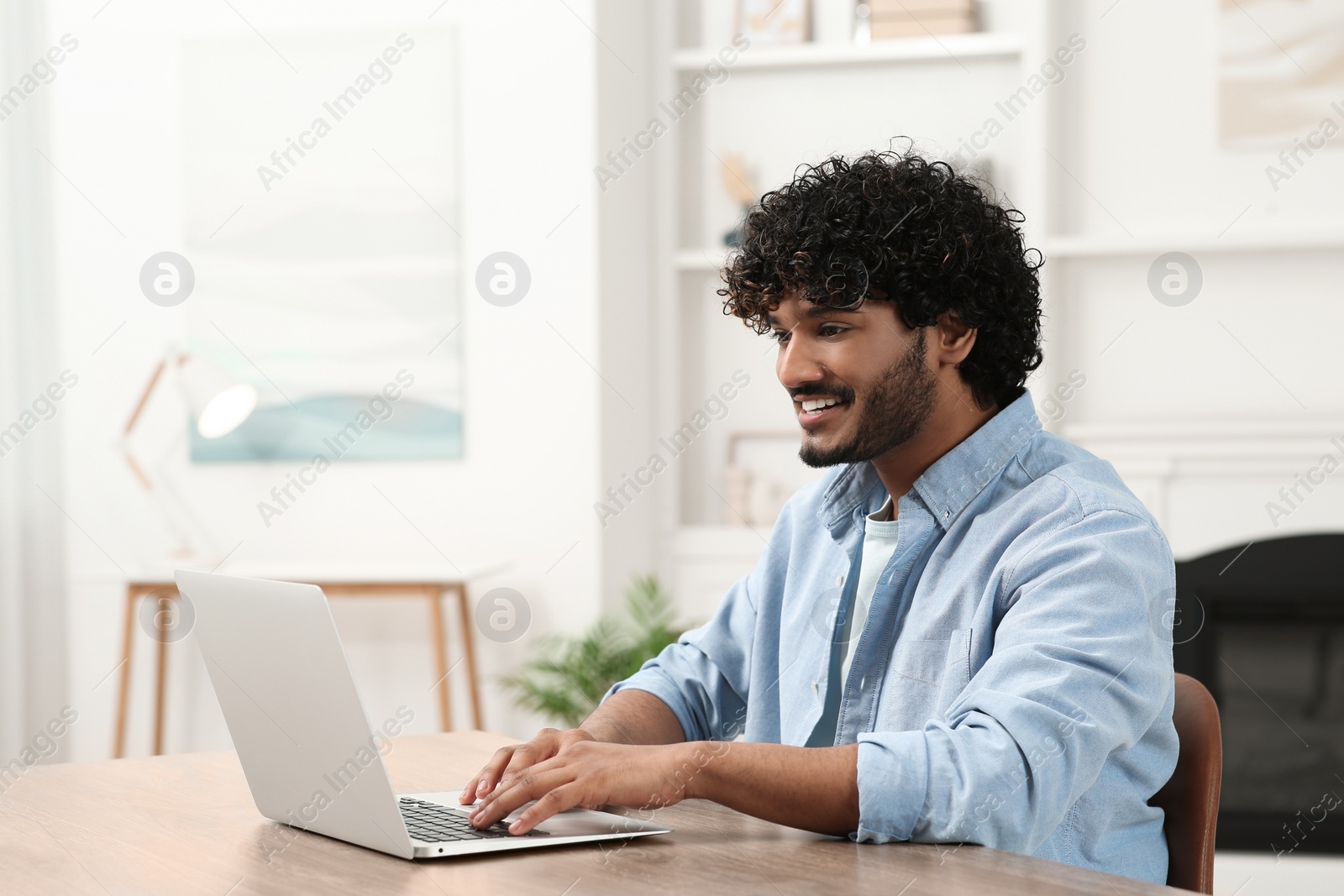 Photo of Handsome smiling man using laptop in room, space for text