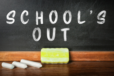 Pieces of white chalk and duster on table near blackboard with text SCHOOL'S OUT