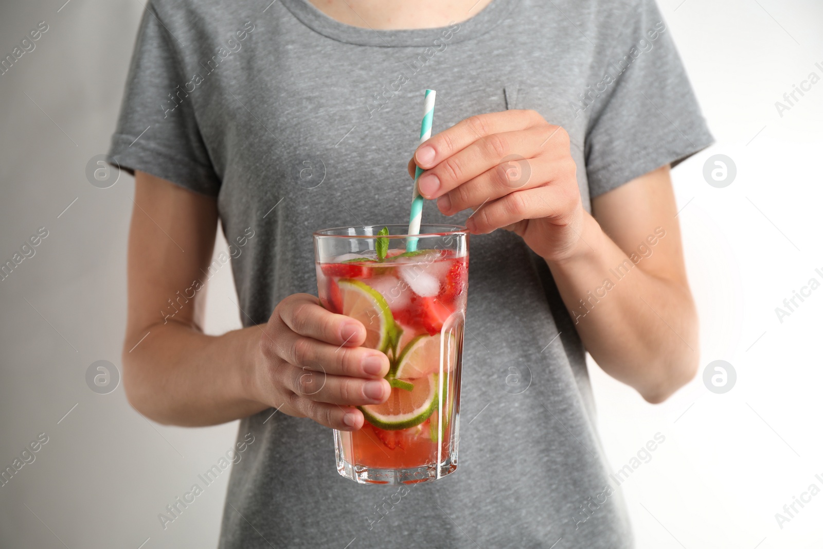 Photo of Young woman with glass of tasty refreshing drink on light grey background, closeup