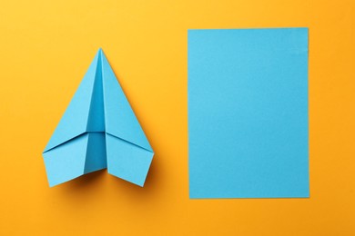 Handmade light blue plane and piece of paper on yellow background, flat lay