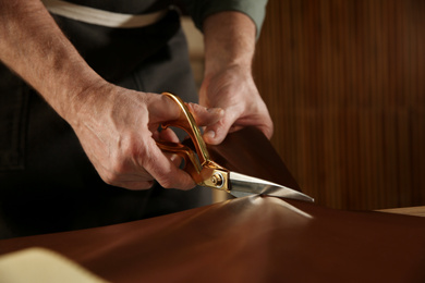 Man cutting leather with scissors in workshop, closeup