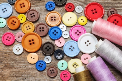 Photo of Colorful buttons and threads on wooden background, top view. Tailoring equipment