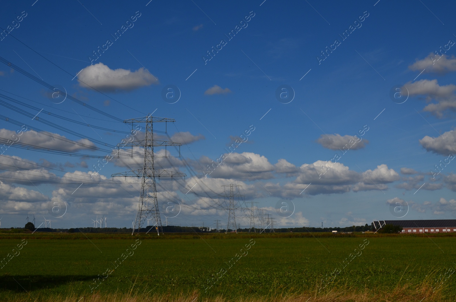 Photo of High voltage towers with electricity transmission power lines in field on sunny day