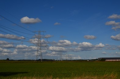 High voltage towers with electricity transmission power lines in field on sunny day