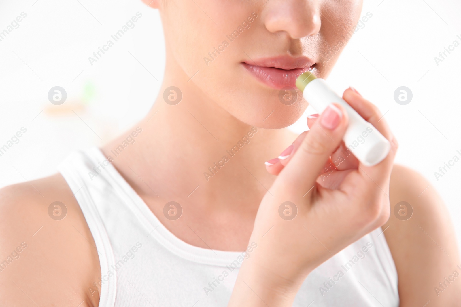 Photo of Young woman applying balm on her lips against light background, closeup