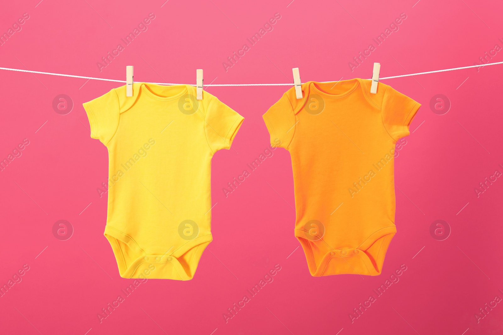 Photo of Baby onesies hanging on clothes line against pink background