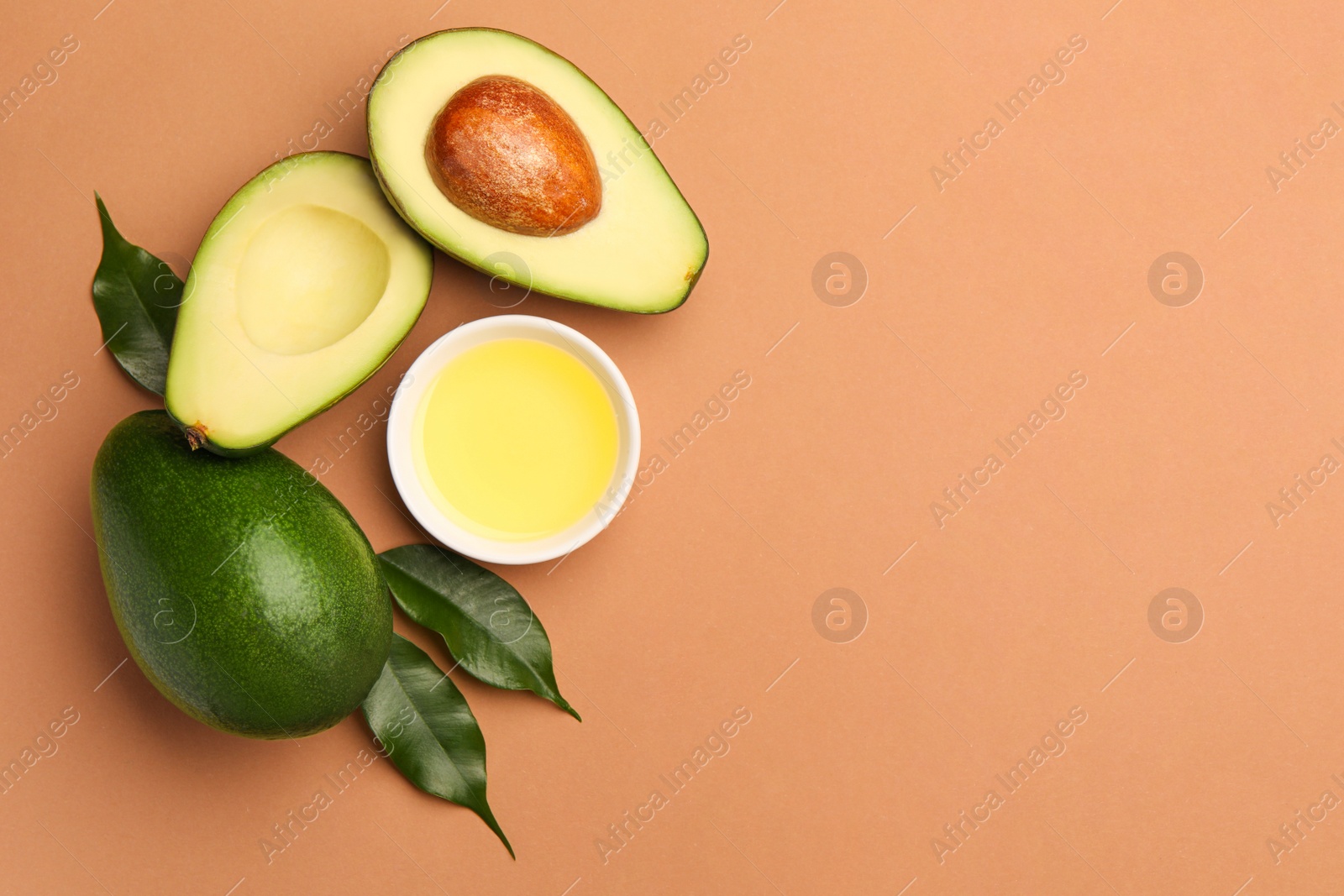 Photo of Cooking oil in bowl and fresh avocados on beige background, flat lay. Space for text