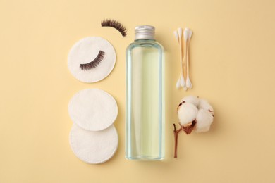 Bottle of makeup remover, cotton flower, pads, swabs and false eyelashes on yellow background, flat lay