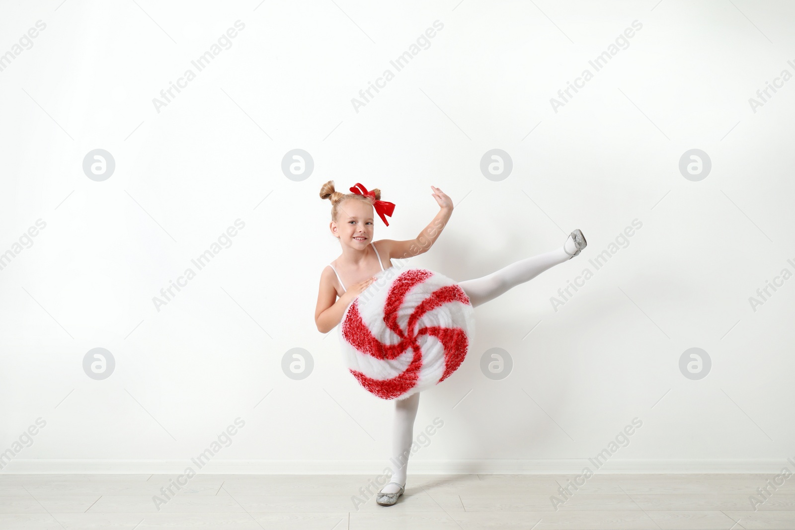 Image of Cute little girl dressed as candy near white wall. Christmas suit