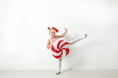 Cute little girl dressed as candy near white wall. Christmas suit