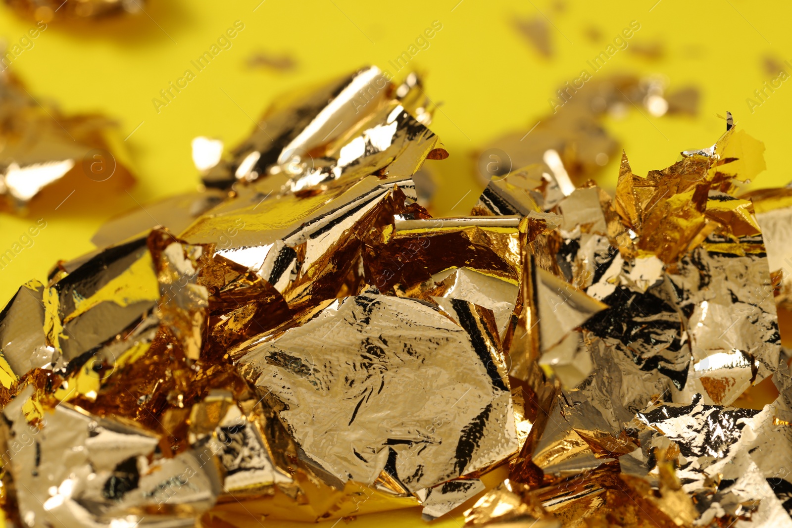 Photo of Edible gold leaf on yellow background, closeup